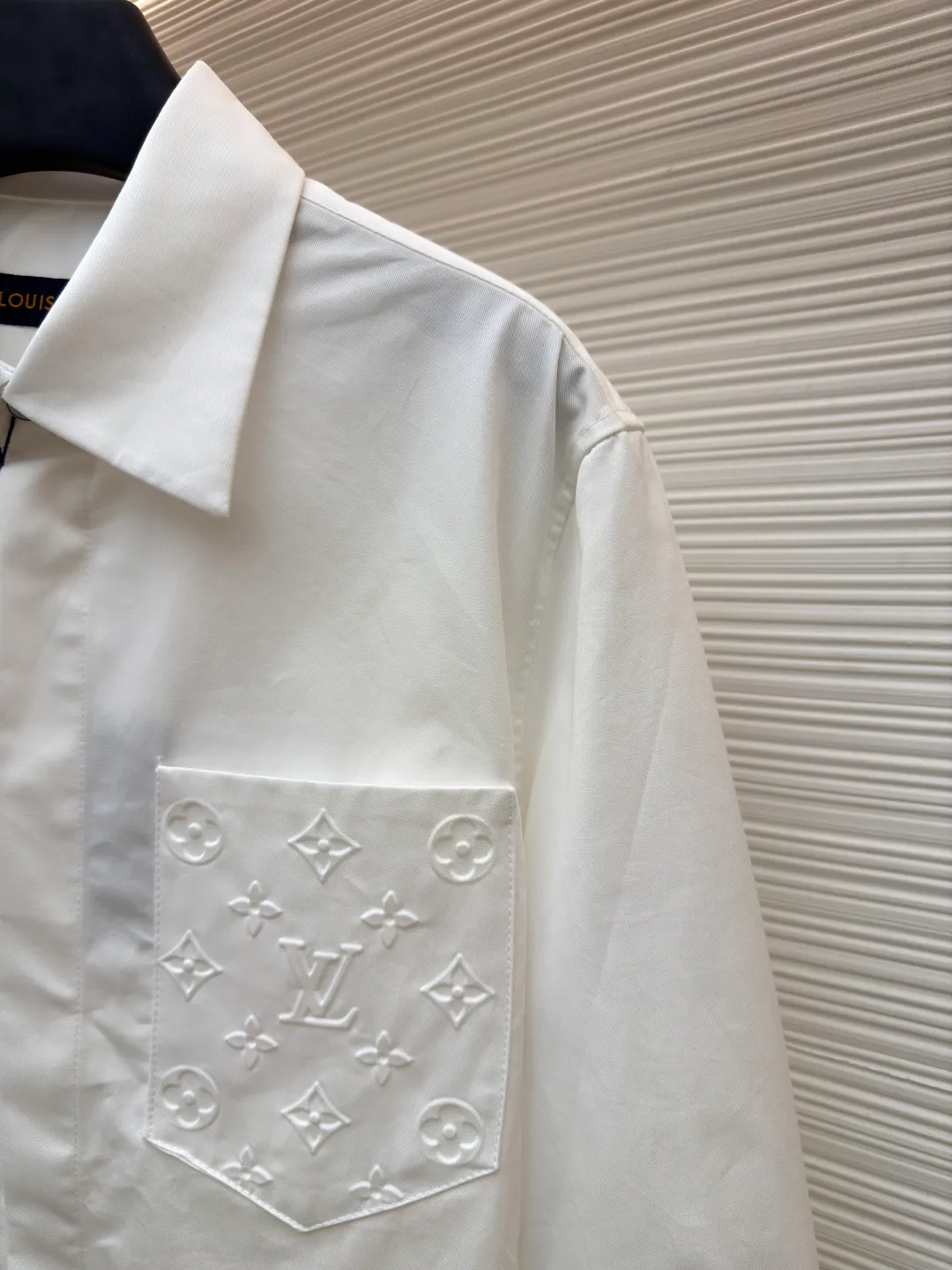 LOUIS VUITTON Embossed Pocket Lapel Shirt ●Original version: Purchased and developed for 3989 ●Item number: 1681491-B05 ●Fabric: Cotton twill woven fabric ●Technology: Concave embossed printing ●Color: white ●Version: Fitted version ●Weight: about 370 grams ●Size: XS-S-M-L ●Description: The twill pattern is obvious on the front of the fabric and blurry on the reverse. Single yarn is used in both warp and weft directions, and the linear density is close. The warp density of the fabric is slightly higher than the weft density, and the hand feel is relatively soft. The fabric has excellent stability, is not easy to deform, and prevents bulging; cotton fiber has good hygroscopicity, which keeps the fabric in a water balance, making people feel comfortable, and adding to the sophistication of the fabric. The concave and convex embossing process is formed by heating and shaping the upper and lower dies. The rollers press the fabric at a certain temperature, and the three-dimensional hierarchical convex surface is produced through mechanical embossing. The fabric produces a concave and convex pattern with a relief-style three-dimensional effect and a special gloss effect. The three-dimensional shape, pattern and text have a strong three-dimensional sense, adding a decorative art effect, clear layers, concentrated three-dimensional image, and accurate perspective angle. The collar can be adjusted with buttons for both formality and comfort; the pleats and tabs at the back are classic shirting techniques, with the pleats providing extra room for movement and the tabs keeping the shirt in shape when hanging. The button front uses custom-fit buttons that are positioned accordingly, and together these details ensure the shirt's functionality and crisp look. The overall wiring is straight and delicate, the fabric is comfortable and soft, and the color is consistent without color difference. It can be matched with the same style to create a fashionable look and control various occasions. Customized accessories, complete with three standards, same style for men and women!
